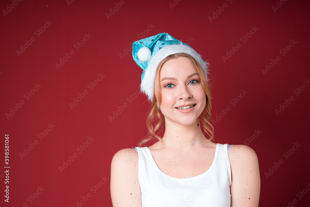 Beautiful blond woman smiling in white tank top and blue christmas hat isolated on red background. Beautiful blond woman smiling in white tank top and blue christmas hat isolated on red background.