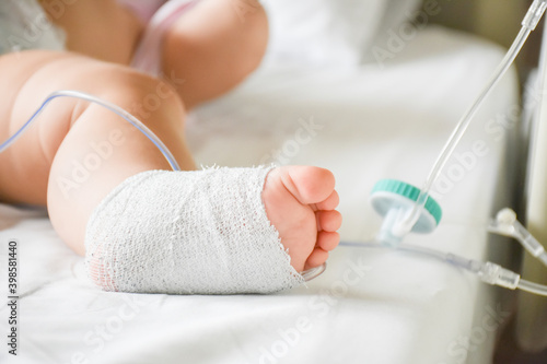 Little sick baby on a drip receiving a saline solution intravenously in the hospital or clinic. Baby with cannula in the feet on a hospital bed