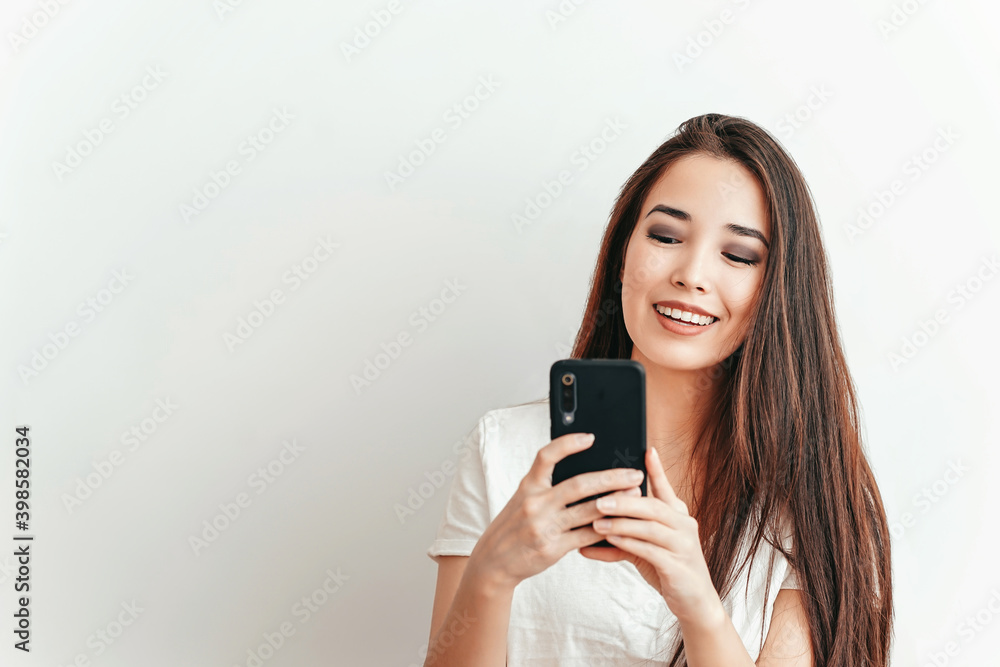 Beautiful Asian smiling girl talks on the phone on a white background in a white t-shirt with a beautiful smile Beautiful Asian smiling girl talks on the phone on a white background in a white t-shirt with a beautiful smile
