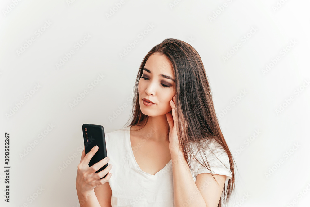 Beautiful Asian smiling girl talks on the phone on a white background in a white t-shirt with a beautiful smile Beautiful Asian smiling girl talks on the phone on a white background in a white t-shirt with a beautiful smile