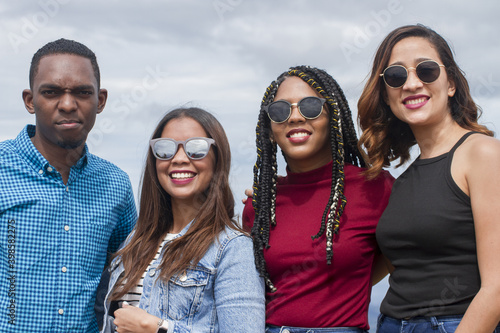 group of four Latin American adventurers friends outdoors smiling and looking to camera using sunglasses half body shot and sky background landscape in dominican republic in a summer day photo