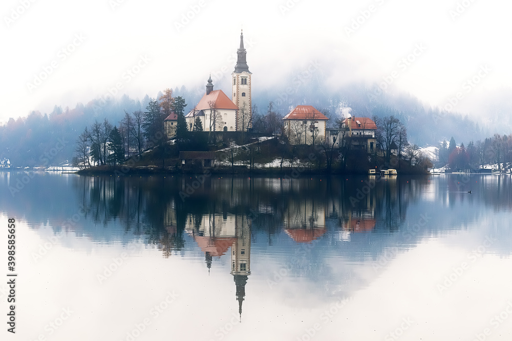 Bled lake in wintertime, scenic view of Bled Island with mountains in fog