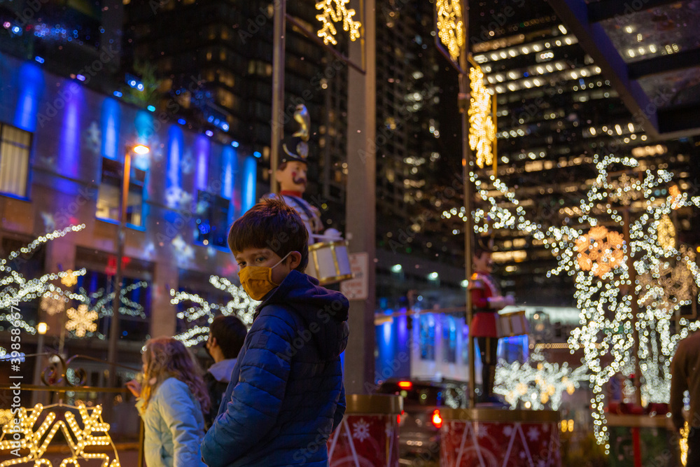 A boy wearing a face mask outside looking at Christmas lights A boy wearing a face mask outside looking at Christmas lights