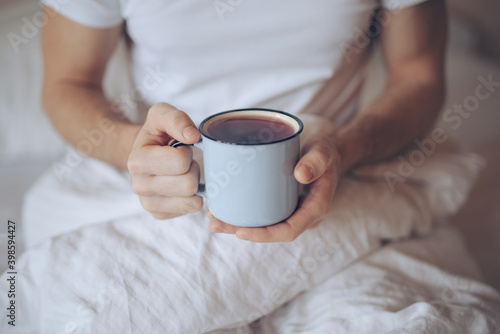 Closeup of man holding cup with tea at the morning in a bed