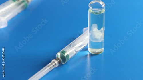 An ampoule with a vaccine and a syringe are on a blue background. The concept of vaccination against coronavirus.