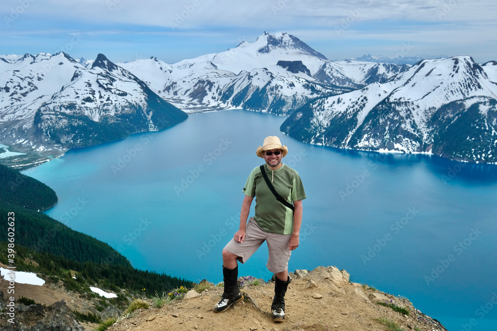 Hiker on the top of mountain above turquoise lake and snowcapped peaks. Garibaldi Lake. Whistler. British Columbia. Canada 