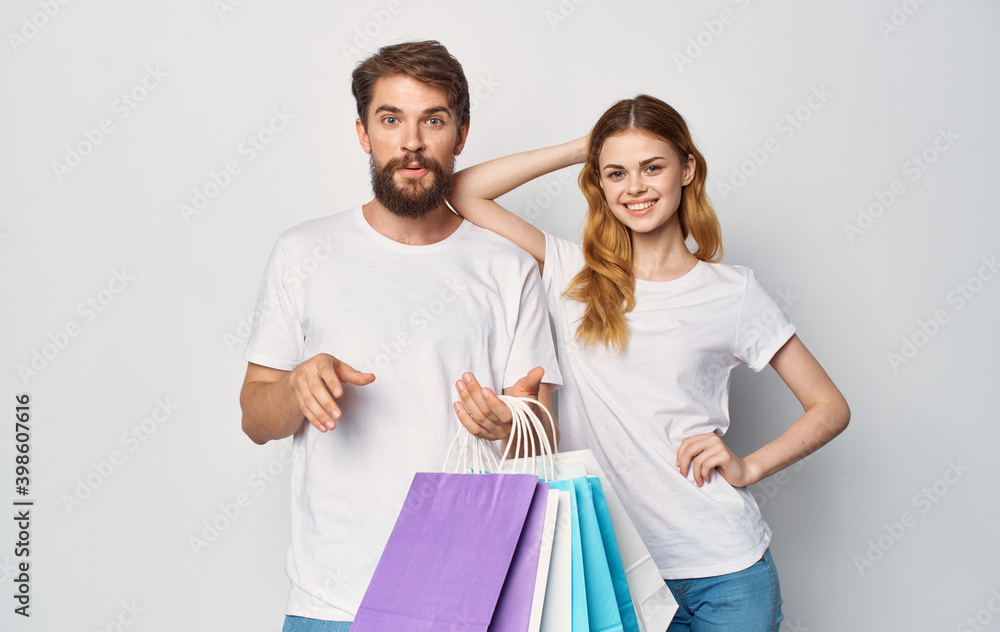 Happy young couple in white T-shirts with packages in hands Shopping is joy Happy young couple in white T-shirts with packages in hands Shopping is joy