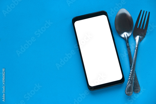 Mockup image of mobile phone, spoon and fork on blue background with copy space.