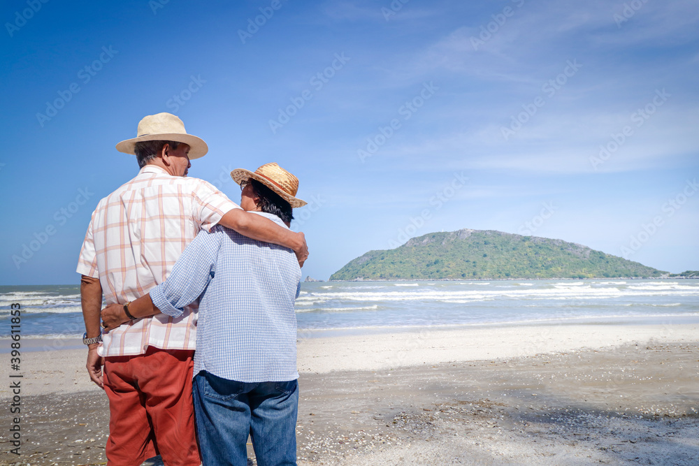 An elderly Asian couple hugging each other on the beach. Look at the beautiful sea. Travel concept Live a happy life in retirement. copy space
