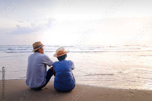An elderly Asian couple sitting on the beach Look at the beautiful sea in the morning together. Travel concept to live happily in retirement age. copy space
