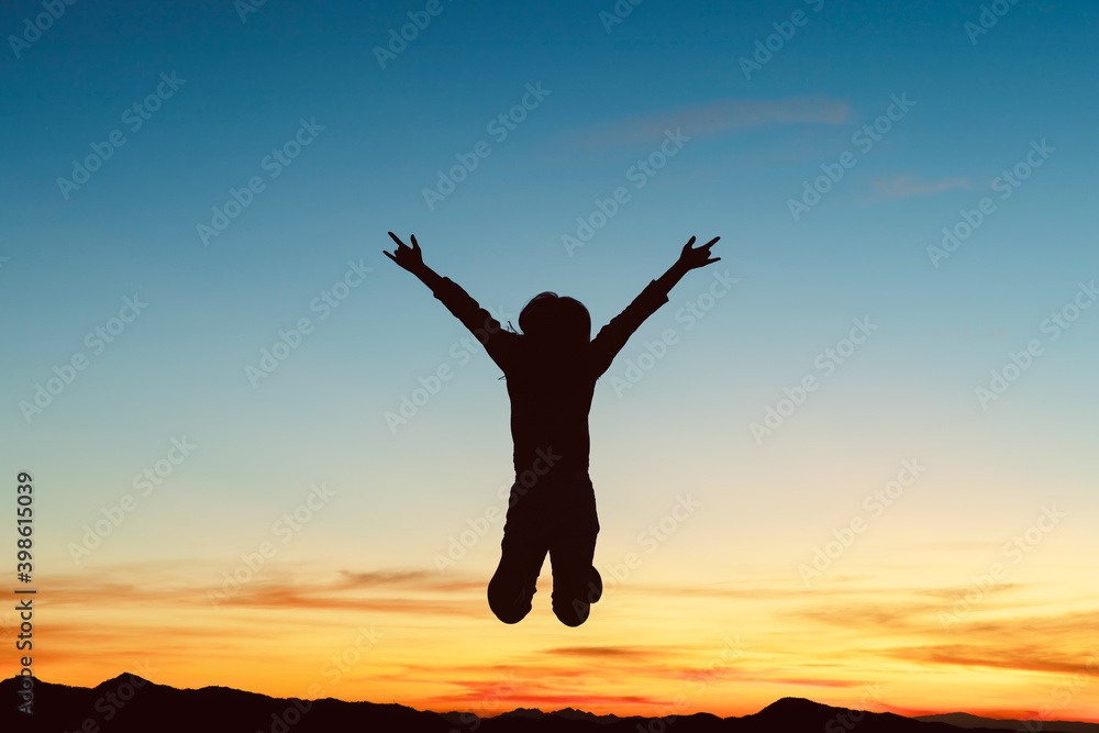 Silhouette of happy girl jumping playing on mountain at sunset