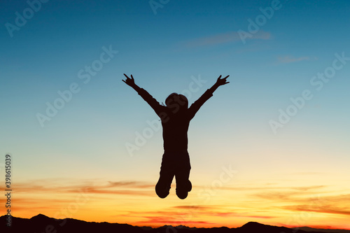 Silhouette of happy girl jumping playing on mountain at sunset