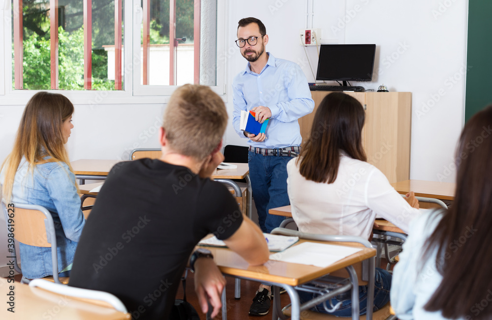 positive young teacher is giving lecture for students with book in the class.