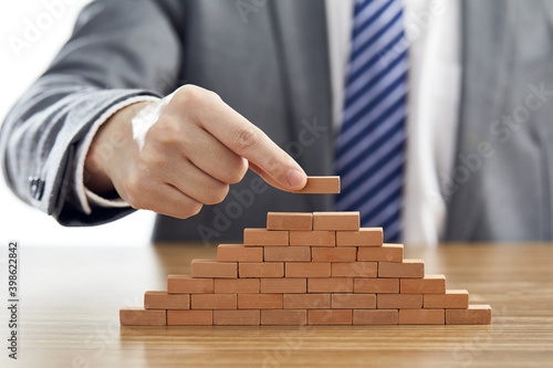 Businessman in a suit putting the last piece of a pyramid using wooden blocks - success concept photo