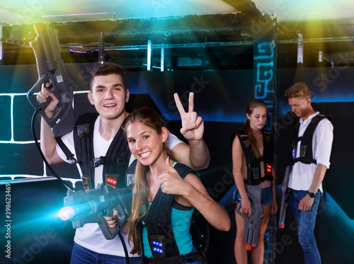 Happy team of laser tag winners guy and girl in foreground and losers team in background