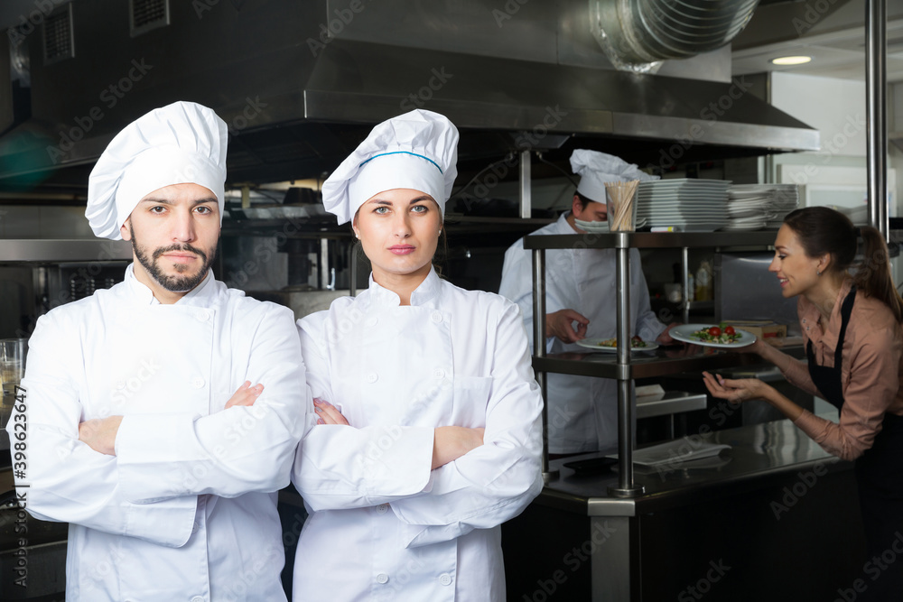 Portrait of confident chefs posing with crossed arms in professional kitchen