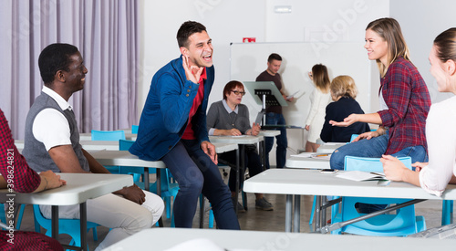 Friendly multinational group of students talking in classroom having break between lessons