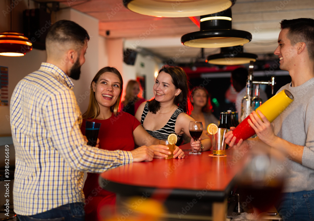 Portrait of happy people and bartender shaking cocktail mixer in nightclub