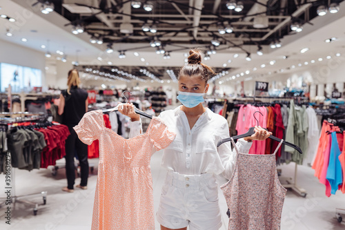 Young woman shopping apparels in clothing boutique with protective face mask