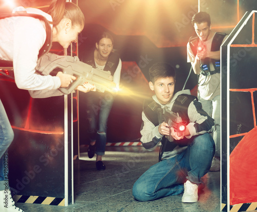 Happy teen boy with laser pistol playing laser tag with friends on dark labyrinth..