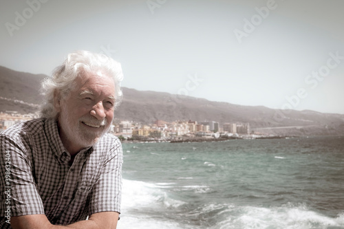 Obraz na plátne Attractive and carefree senior man with beard and white hair  leaning against th