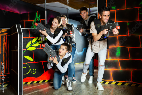 Group of adult friends with laser guns having fun on dark lasertag arena