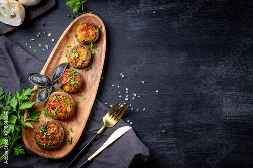 Foto Baked stuffed mushrooms on a wooden plate and black background, top view, copy