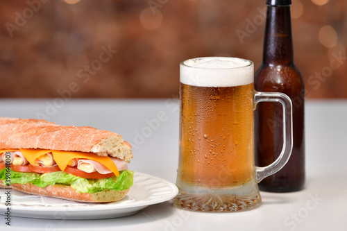 view of a mug of beer next to a delicious looking sub sandwich with meat and vegetables
