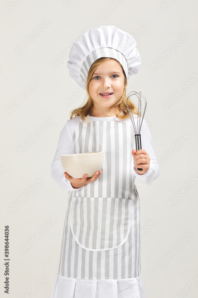 smiling little girl in chef hat and apron with bowl and whisk. child dreams of becoming a chef smiling little girl in chef hat and apron with bowl and whisk. child dreams of becoming a chef