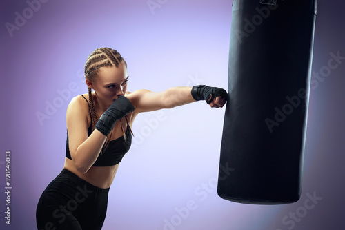 sporty brunette woman with boxing bandages in sportswear hitting the boxing bag on smoke background © producer