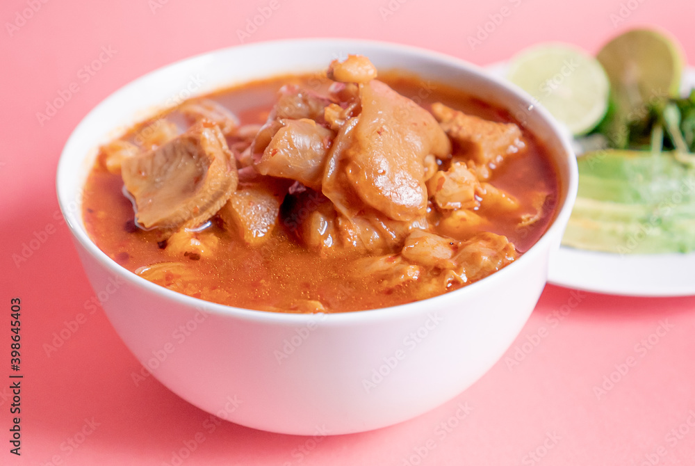 Exquisite Mexican Menudo on a white plate accompanied by a dish with condiments on the back. Exquisite Mexican Menudo on a white plate accompanied by a dish with condiments on the back.