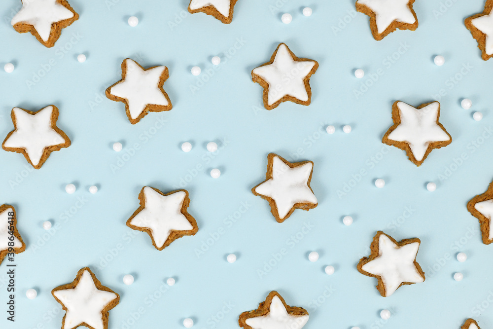 Top view of German star shaped glazed cinnamon Christmas cookies called 'Zimtsterne' on light blue background with snowball ornaments Top view of German star shaped glazed cinnamon Christmas cookies called 'Zimtsterne' on light blue background with snowball ornaments