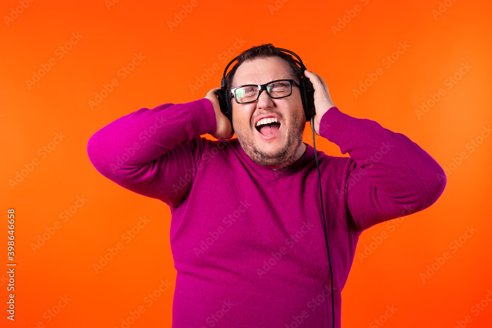 Fototapeta premium Relaxed funny thick man, dances while listens music, moves arms and closes eyes in enjoyment, wears headphones on ears, has fun and feels aspiration.