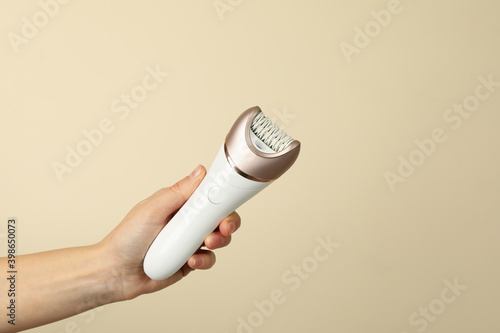Female hand hold epilator on beige background, space for text photo
