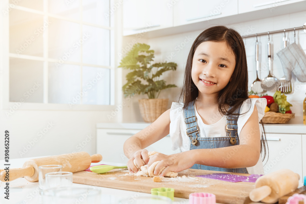 Cute little girl are kneading dough and smiling while preparing it for baking in kitchen at home. Cute little girl are kneading dough and smiling while preparing it for baking in kitchen at home.
