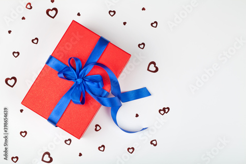 red gift or present box with blue ribbon and heart confetti on white background. photo