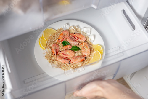 Women's hands are taking out a plate of rice, shrimps and lemon from the freezer of the fridge. Concept of ready made frozen dishes and saving time on cooking food