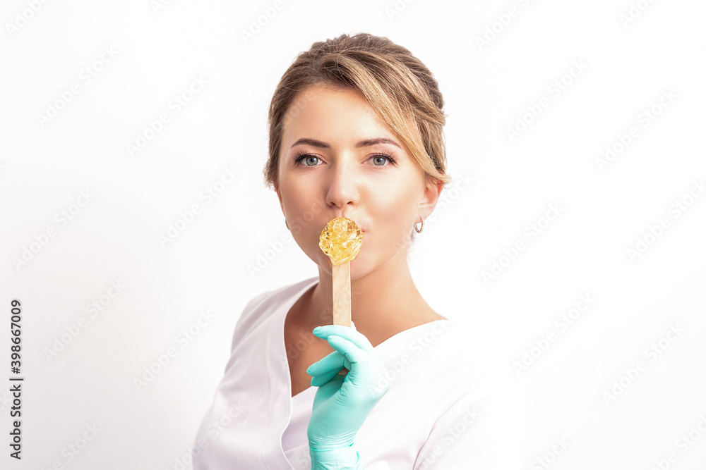 Portrait of female cosmetologist holds a wooden stick with a wax covering her lips on white background Portrait of female cosmetologist holds a wooden stick with a wax covering her lips on white background