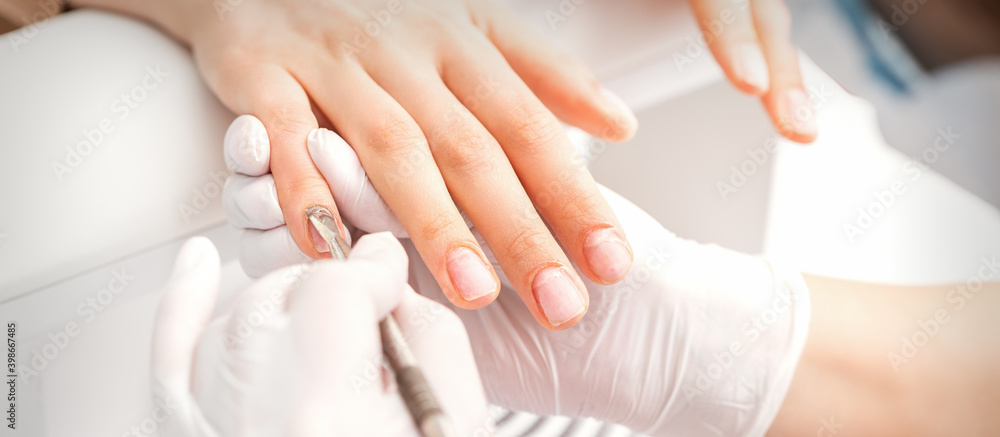 Closeup of beautiful woman's fingernails receiving cleaning cuticle with manicure pusher tool while getting a manicure Closeup of beautiful woman's fingernails receiving cleaning cuticle with manicure pusher tool while getting a manicure