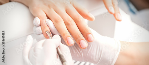 Closeup of beautiful woman s fingernails receiving cleaning cuticle with manicure pusher tool while getting a manicure