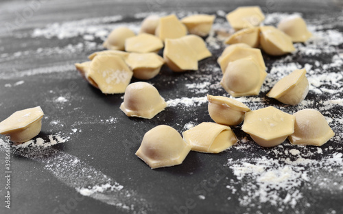 Dumplings, ravioli close-up, hexagonal shape of dough on a black table. Dusted with flour.