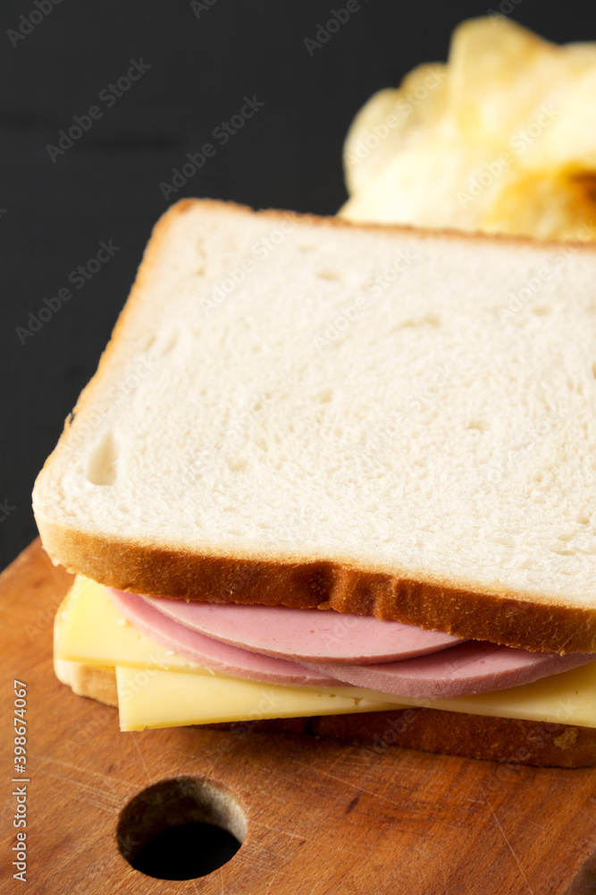 Homemade Bologna Cheese Sandwich with Chips on a rustic wooden board on a black background, side view.