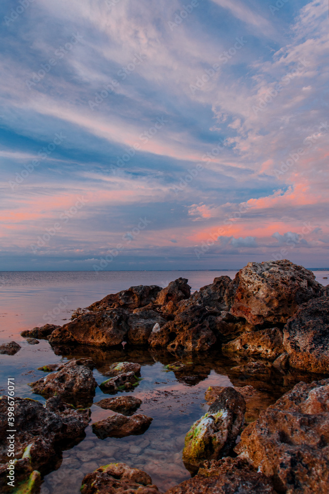 The pink sunset sky is reflected in the sea surface. Rocks and sea.