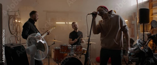 WIDE Friends playing music during their rock band rehearsal repetition inside a garage. Vocals, guitars and drums. Shot with 2x anamorphic lens