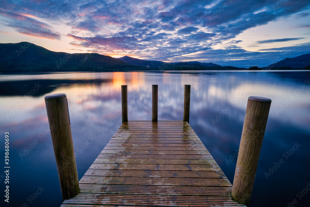 Vibrant sunset with dramatic clouds and wooden jetty at Derwentwater Lake in the Lake District, UK.