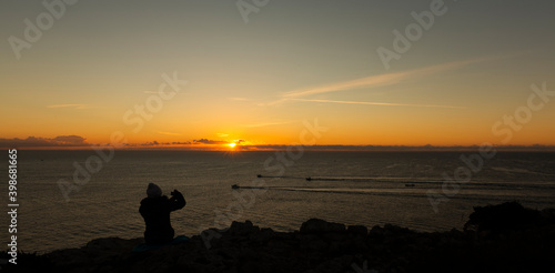 Woman sitting on a cliff, taking photos of the landscape
