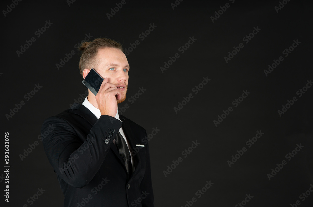 Portrait of young smart confident and successful businessman in black suit using smartphone isolated on black background