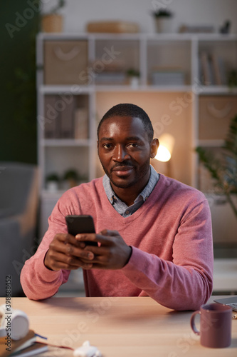 Portrait of African businessman looking at camera while working online on his mobile phone sitting at the table