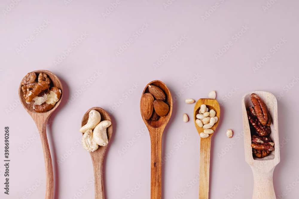 Wooden spoons with pecans, walnuts, almonds and other nuts on pink backround Wooden spoons with pecans, walnuts, almonds and other nuts on pink backround