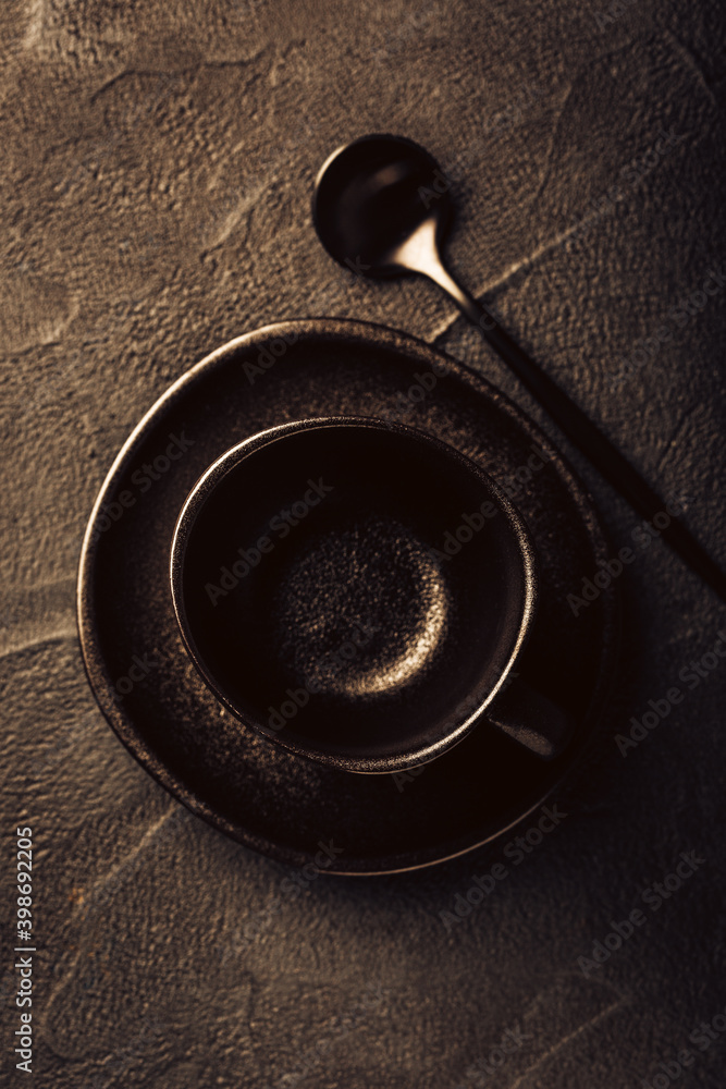 Black coffee cup, saucer and spoon on black texture background. Top view and copy space